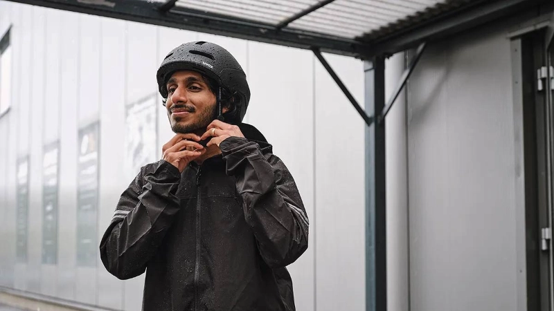 Ein Mann mit Regenmantel zieht sich einen schwarzen Helm auf und steigt auf sein Fahrrad Ein Mann mit Regenmantel zieht sich einen schwarzen Helm auf und steigt auf sein Fahrrad