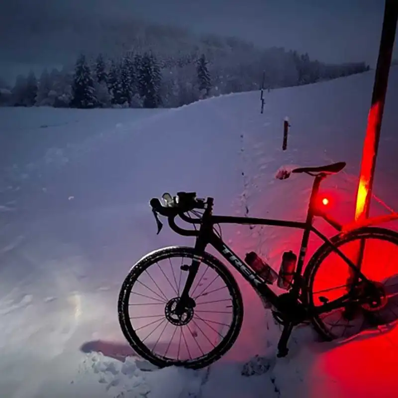 Ein Mountainbike auf verschneitem Feldweg, in der Dämmerung leuchtet das Rücklicht rot auf dem Schnee Ein Mountainbike auf verschneitem Feldweg, in der Dämmerung leuchtet das Rücklicht rot auf dem Schnee